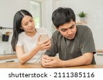 Small photo of Infidelity, suspicion asian young couple love fight relationship, wife holding cellphone, smartphone cheating on phone, scolding husband about mistrust, distrust and jealousy when sitting at home.