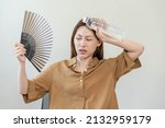 Summer heat stroke, hot weather, tired asian young woman sweaty and thirsty, refreshing with hand in blowing, wave fan to ventilation, holding cold water bottle tap her body when temperature high.