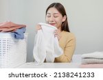 Small photo of Feel softness, smiling asian young woman, girl touching fluffy towel cotton, smelling fresh clean clothes on table after washing, laundry, dry. Household working at home. Laundry and maid.