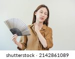Suffering summer heat stroke, hot weather, tired asian young woman, girl sweaty and thirsty, refreshing with hand in blowing, wave fan to ventilation when temperature high at home, house.on background