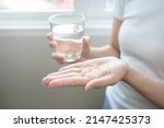 Small photo of Dietary Supplement, Nutrition asian woman, young hand in holding yellow pill, talking daily vitamin D, E, A, fish oil pill for hair and skin with glass of water. Diet healthy eating, beauty people.
