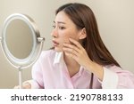 Small photo of Dermatology, expression face worry asian young woman looking mirror hand touch facial at dark spot of melasma, freckles from pigment melanin, allergy sun. Beauty care, skin problem treatment, skincare