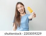 Cheerful enjoy, happy cute asian woman wearing casual with brunette hair, eating popsicle, teenage girl holding ice pop, lolly frozen stick with mango yellow, passion fruit ice cream tasty in summer.