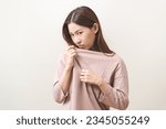 Small photo of Bad smelling, deodorant asian young woman smell stink, breathing nose smelly on shirt dirty stinky laundry, disgusting from clothes after washed, smelly armpit underarm Medical health, skin body care.