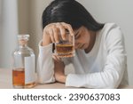 Alcoholism drunk asian young woman hand holding glass of alcohol or whiskey, female sitting alone, drinking on table at home, at night. Treatment of alcohol addiction, suffer abuse problem alcoholism