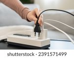 Small photo of Closed up hand of woman plugged in, unplugged electricity cord cable on socket on table for energy saving, electric power on plate outlet, control expense electrical appliances, environment concept.