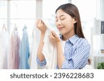 Small photo of Feel softness, hygiene. Smile asian young woman touching fluffy white shirt smelling fresh clean clothes, pretty girl comfort sniff after washing laundry. Household work at home, chore of maid concept
