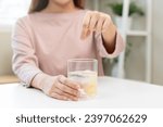 Small photo of Close up young woman hand putting or dropping effervescent tablet into glass of water, holding pain pill, painkiller medicine, aspirin for treatment, take vitamin c for hangover. Health care concept.