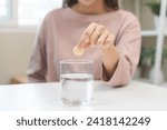 Small photo of Smile asian young woman putting or dropping effervescent tablet into glass of water, holding pain pill, painkiller medicine, aspirin for treatment, take vitamin c for hangover. Health care concept.