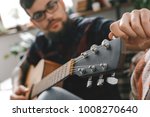 Young guitarist hipster at home with guitar fixing tuning pegs close-up