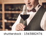 Senior man sommelier standing near cabinet holding glass smelling red wine close-up concentrated