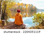 Small photo of Lonely woman is sitting on the shore of a forest lake. Autumn landscape, calmness, tranquility, travel.