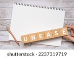 Small photo of Wooden blocks with "UNEASE" text of concept, a pen, and a notebook.