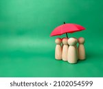 A group of wooden dolls are hiding under a red umbrella, protecting wooden peg dolls, planning, saving families, preventing risks and crises, health care and insurance concepts.