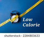 Measuring tape and alarm clock with the word Low Calorie on blue background.