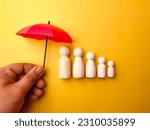 Small photo of A group of wooden statues are lining up to take shelter under a red umbrella held by someone on a yellow background