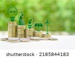 Alternative or renewable energy financing program, financial concept : Green eco-friendly or sustainable energy symbols atop five coin stacks e.g a light bulb, a rechargeable battery, solar cell panel