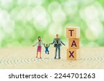 Small photo of High income child benefit tax charge, financial concept : Couple holds a toddler near wood cubes with the word TAX written on them on a maze. Depicting a trap in which households pay a greater tax.