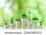 Small photo of Renewable or clean energy generation prices and costs, financial concept : Green eco-friendly symbols atop coin stacks e.g. energy efficient light bulb, a battery, a solar cell panel, a wind turbine.