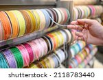 Small photo of Male hand choosing gray Ric Rac ribbon from colorful ribbon rack in craft shop. Artisan and Handcraft concept