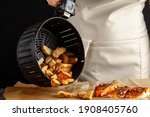 Small photo of A caucasian woman chef is dumping fresh made fried potato chunks on a piece of baking paper which has three oven roasted marinated salmon fillet with basil and pepper on top. Homemade fish and chips.