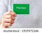 Small photo of A young caucasian woman is holding a green card that says member on it. A customizable image which has space for text to be inserted. Being a member, membership dues, subscription, group concepts.