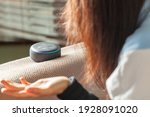 Small photo of Clarksburg, MD, USA 03-01-2021: A caucasian woman sitting on an armchair with casual clothes in her house is asking a question to Amazon Echo Dot, voice activated speaker device.