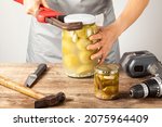 A funny quirky concept image showing a caucasian woman trying to open a jar of pickles. She is trying with tools like drill, knife, wrench and hammer 