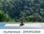 Small photo of The girl testifies sitting on the rug in the lotus position on the background of the tropical jungle. Back view