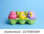 Cute easter eggs with funny faces in green box isolated on light blue background. Happy easter concept. Painted Easter eggs.