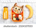 Funny owl sandwich with cheese and ham and egg in shape of rabbit. Orange juice in a glass bottle and a banana. School lunch box for kids. Top view. Copy space