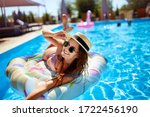 Young smiling fitted girl in bikini, straw hat relax on inflatable swan in swimming pool. Attractive woman in swimwear lies in the sun on tropical vacation. Pretty female sunbathing at luxury resort.