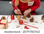 Small child wearing Christmas holiday pajamas, doing crafts, painting Christmas tree decorations, sitting at table. DIY and handmade concept.
