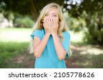 Small photo of Vivacious caucasian little girl wearing blue t-shirt standing outdoors , giggles joyfully, covers mouth, has natural laughter, hears positive story or funny anecdote