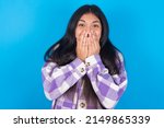 Small photo of Vivacious young hispanic woman wearing plaid shirt over blue background , giggles joyfully, covers mouth, has natural laughter, hears positive story or funny anecdote