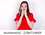 Small photo of Vivacious young caucasian woman wearing red T-shirt over white background, giggles joyfully, covers mouth, has natural laughter, hears positive story or funny anecdote