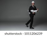 Small photo of Full length portrait of troublous bearded builder holding rolls of paper while in hurry to work. Profession concept. Copy space