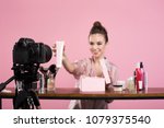 Famous blogger. Cheerful female vlogger is showing cosmetics products while recording video and giving advices for her beauty blog. Focus on digital camera