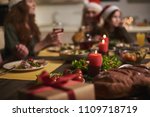 Focus of festive table decorated with candles for Christmas. Two women are sitting at background with kid eating vegetables and drinking red wine