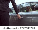 Small photo of Considerate hotel worker on duty reaching for the car door helping accommodate guests arrival and overall vacation experience