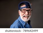 Small photo of Portrait of jocular old male in cap making funny wry face and winking. Isolated on grey background