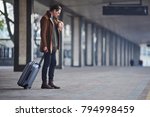 What time is it. Full length side view serious man looking at modern watch while keeping big suitcase. He waiting for train. Trip concept