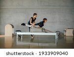 Small photo of Full shot of Woman doing core exercises during Personal Pilates class on a Reformer machine, by a female instructor at a big gymnasium center, wide industrial studio. Healthy fitness lifestyle.