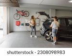 Small photo of Son plugs EV charger from charging station to electric vehicle in private home while mother takes groceries from the car on daytime. Sustainable Alternative Lifestyle. Horizontal copy-space.