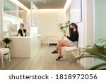 Patient waiting at the reception of the dental, gynecological or aesthetic clinic. The patient is using her smartphone while the receptionist takes a call. Medical concept.