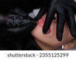 Small photo of Permanent make-up procedure for the lips, the master stretches the lips and applies permanent make-up. Delicate permanent lip makeup for blondes