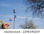 Small photo of Male holding Netherland flag with in background pole of acoustic air alarm system also known as air raid siren alert aka luchtalarm in Dutch in Holland to warn public for example during war or attack