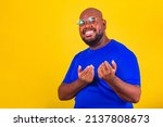 Small photo of handsome afro brazilian man wearing glasses, blue shirt on yellow background. sign come, come, come here, here, welcome, receptive, reception. getting. gesture come.