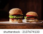 Small photo of Two hamburgers on a wooden background. Big and small cheeseburger. Hamburger day.