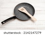 Frying pan with non-stick ceramic coating and spatula on a white wooden background. Cooking without sticking or oil.